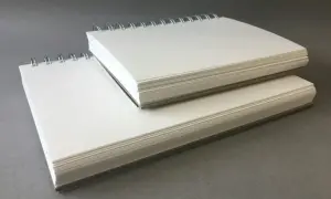 Deux carnets à spirales empilés, remplis de papier pour acrylique blanc épais, prêts pour la création artistique.