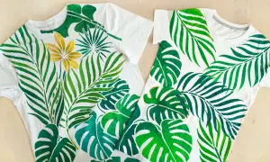Deux tee-shirts blancs ornés d'une peinture de feuilles tropicales vertes et d'une fleur dorée.
