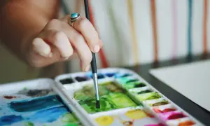 Main d'une artiste utilisant la technique pastel sec pour mélanger des couleurs vives sur une palette.