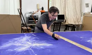 Un artiste stylo bic travaille sur une grande toile bleue, créant un motif d'étoiles filantes.