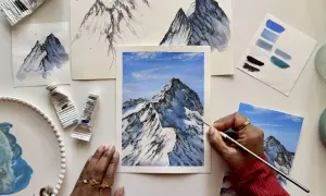 Apprendre comment faire du blanc avec de la gouache pour peindre des montagnes enneigées. Des tubes de peinture, des études et une œuvre en cours sont visibles.