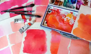 Des carrés de feutre aquarelle aux teintes roses et orangées, des tubes de peinture et des pinceaux. L'utilisation du feutre aquarelle est mise en avant.