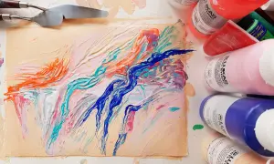 Peinture abstraite aux couleurs vives sur un support, avec des spatules et des tubes de peinture acrylique.