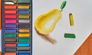 Un dessin au pastel d'une poire jaune avec une feuille verte. Des pastels de différentes couleurs sont disposés à côté.