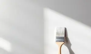 Pinceau neuf prêt à appliquer une peinture pour plastique sur une surface blanche, avec des ombres douces projetées par la lumière.