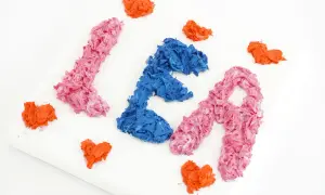 Peinture avec les mains : les lettres "LÉA" en relief, rose et bleu, entourées de cœurs orange sur une toile blanche.