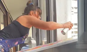 Artiste en salopette peinte, expérimentant comment peindre sur une toile déjà peinte avec une bombe aérosol.