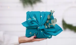Préparer Noël : un cadeau joliment emballé dans un tissu bleu canard orné de motifs dorés, décoré d'une branche d'eucalyptus.