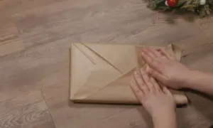 Emballage cadeau livre en papier kraft, prêt pour Noël. Les mains ajustent les plis pour une finition parfaite.