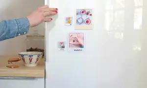 Main d'une femme plaçant des photos sur un frigo, une idée pour fabriquer des magnets frigo personnalisés.