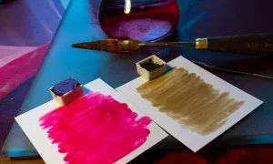 Des petits pots de peinture acrylique, un pourpre intense et un brun terreux, prêts à mélanger pigments. Une spatule et un flacon de liquide rouge complètent la scène.
