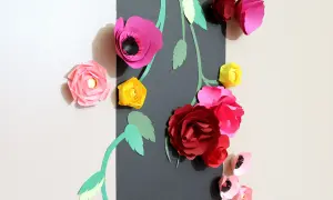Un bouquet de fleurs en papier Canson aux couleurs vives, roses, rouges et jaunes, orne un mur.