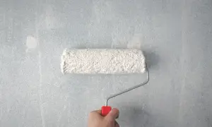 Main tenant, voici comment faire la peinture : un rouleau blanc couvre un mur bleu clair.