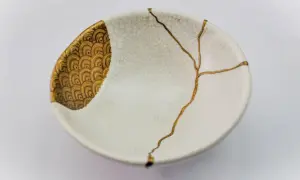 Bol blanc orné de motifs dorés, réparé avec l'art japonais de la vaisselle cassée, soulignant la beauté des imperfections.