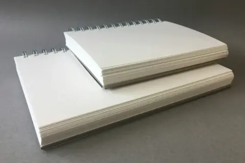 Deux carnets à spirales empilés, remplis de papier pour acrylique blanc épais, prêts pour la création artistique.