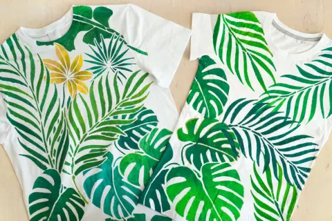 Deux tee-shirts blancs ornés d'une peinture de feuilles tropicales vertes et d'une fleur dorée.