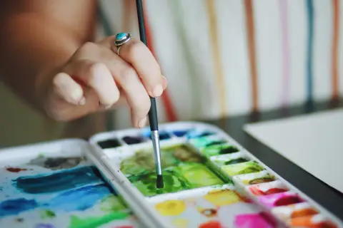 Main d'une artiste utilisant la technique pastel sec pour mélanger des couleurs vives sur une palette.