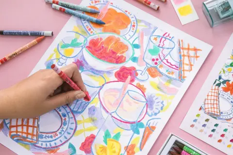 Une main colorie une scène de repas avec des pastels. Une idée art créatif pour un moment joyeux et coloré.