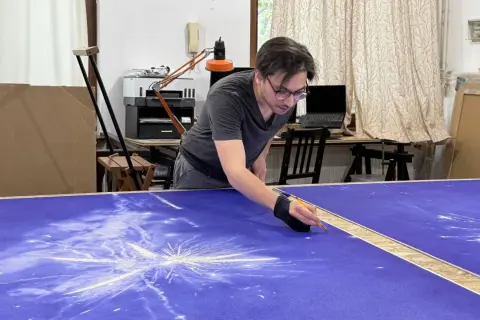 Un artiste stylo bic travaille sur une grande toile bleue, créant un motif d'étoiles filantes.
