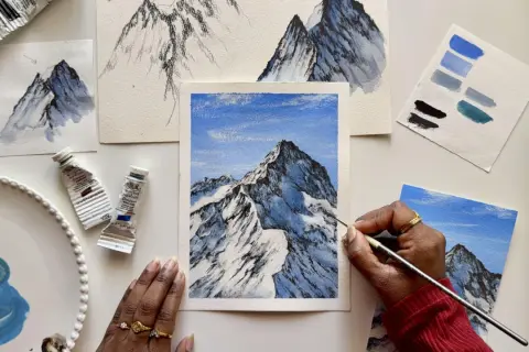 Apprendre comment faire du blanc avec de la gouache pour peindre des montagnes enneigées. Des tubes de peinture, des études et une œuvre en cours sont visibles.