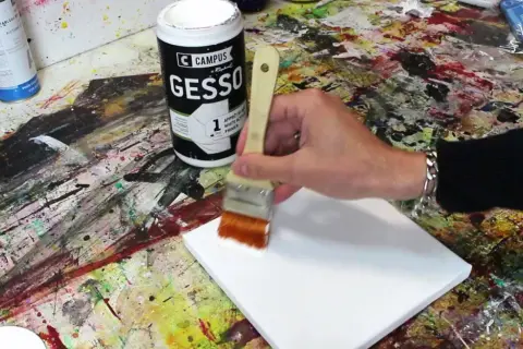 Préparation d'une toile pour peindre. On utilise un pinceau pour mélanger gesso et peinture acrylique, créant une base parfaite pour l'art.