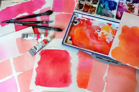 Des carrés de feutre aquarelle aux teintes roses et orangées, des tubes de peinture et des pinceaux. L'utilisation du feutre aquarelle est mise en avant.