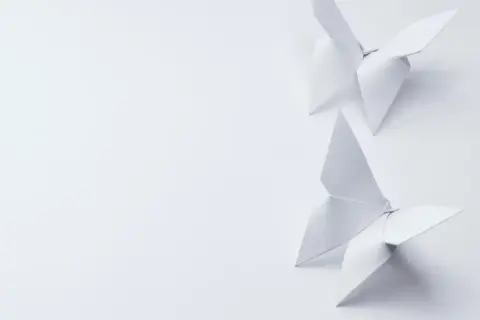 Deux papillons en origami blanc, créés avec un grammage papier origami idéal, flottent sur un fond épuré.