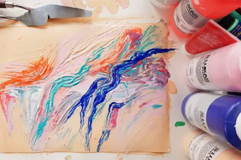 Peinture abstraite aux couleurs vives sur un support, avec des spatules et des tubes de peinture acrylique.