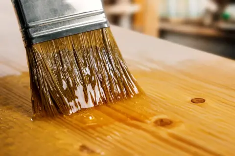 Un pinceau applique du vernis sur une planche de bois. Le vernis brillant reflète la lumière. Quel pinceau pour vernis bois ?
