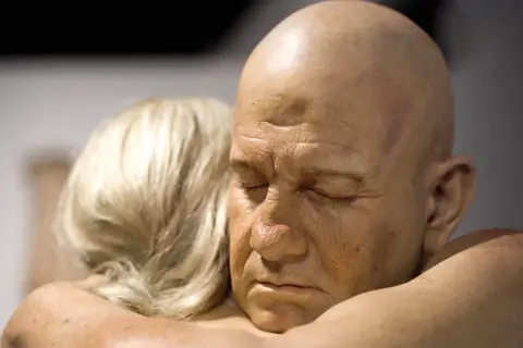 Un homme chauve aux yeux clos est étreint par une femme aux cheveux blonds. Une œuvre saisissante d'un peintre hyperréaliste français.