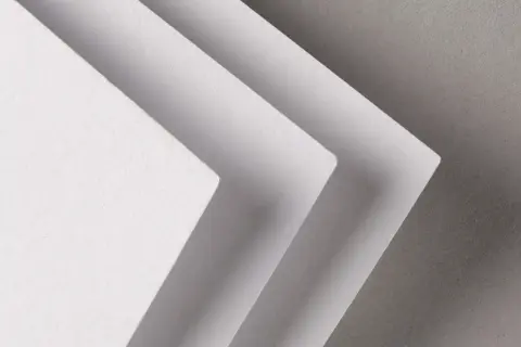 Trois feuilles de papier blanc superposées, créant un effet d'escalier. La texture du papier rappelle celle d'un **format raisin** pour une œuvre d'art.