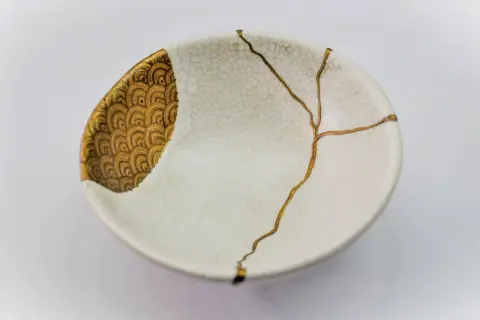 Bol blanc orné de motifs dorés, réparé avec l'art japonais de la vaisselle cassée, soulignant la beauté des imperfections.