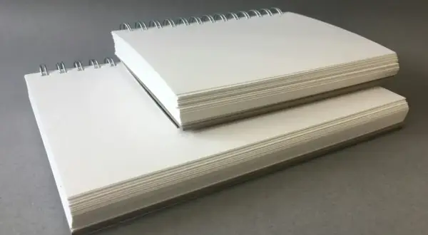 Deux carnets à spirales empilés, remplis de papier pour acrylique blanc épais, prêts pour la création artistique.