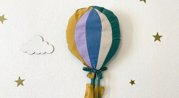 Gabarit patron montgolfière papier, cousu main, prêt à décorer une chambre d'enfant. Nuages et étoiles dorées l'accompagnent.