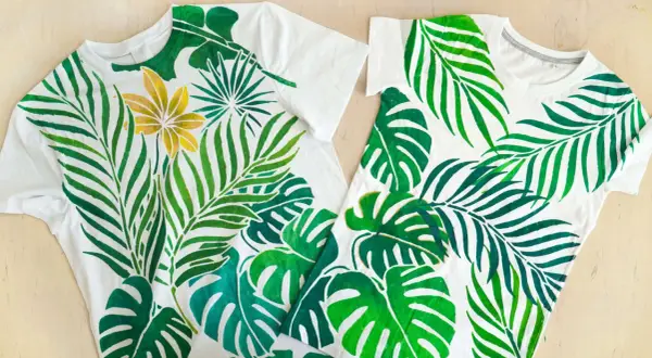 Deux tee-shirts blancs ornés d'une peinture de feuilles tropicales vertes et d'une fleur dorée.