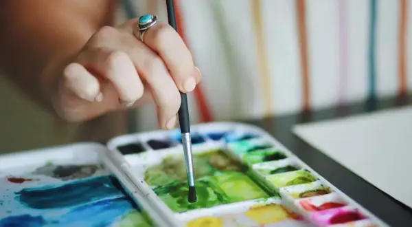 Main d'une artiste utilisant la technique pastel sec pour mélanger des couleurs vives sur une palette.