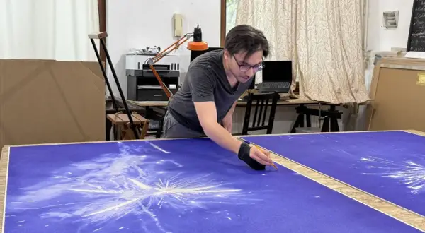 Un artiste stylo bic travaille sur une grande toile bleue, créant un motif d'étoiles filantes.