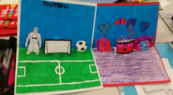Un dessin pop up de football avec un joueur, un ballon et un but. L'autre partie montre un gâteau d'anniversaire, des cadeaux et des cœurs.