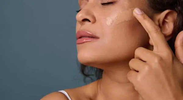 Une femme applique du fond de teint sur sa joue. La **peinture sur la peau** est une étape clé pour un teint parfait.