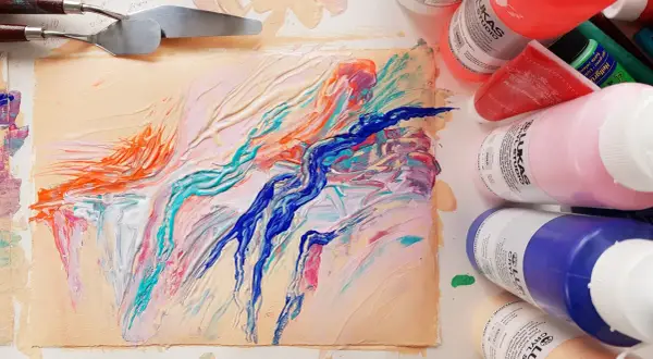 Peinture abstraite aux couleurs vives sur un support, avec des spatules et des tubes de peinture acrylique.