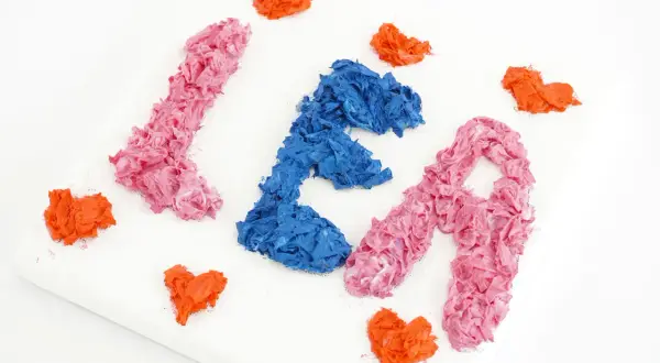 Peinture avec les mains : les lettres "LÉA" en relief, rose et bleu, entourées de cœurs orange sur une toile blanche.
