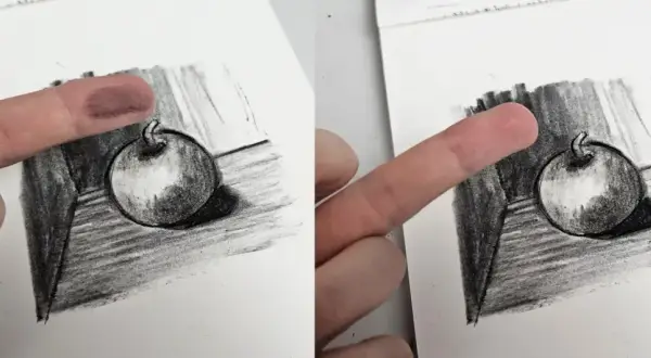 Un doigt est utilisé pour estomper un dessin au fusain d'une pomme, technique d'un artiste connu.