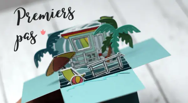 Carte pop-up plage avec cabine de sauveteur, palmier, parasol et transat.
