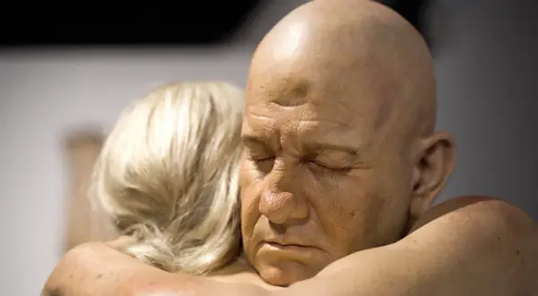 Un homme chauve aux yeux clos est étreint par une femme aux cheveux blonds. Une œuvre saisissante d'un peintre hyperréaliste français.