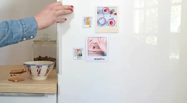 Main d'une femme plaçant des photos sur un frigo, une idée pour fabriquer des magnets frigo personnalisés.