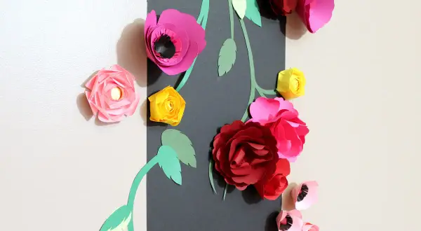Un bouquet de fleurs en papier Canson aux couleurs vives, roses, rouges et jaunes, orne un mur.
