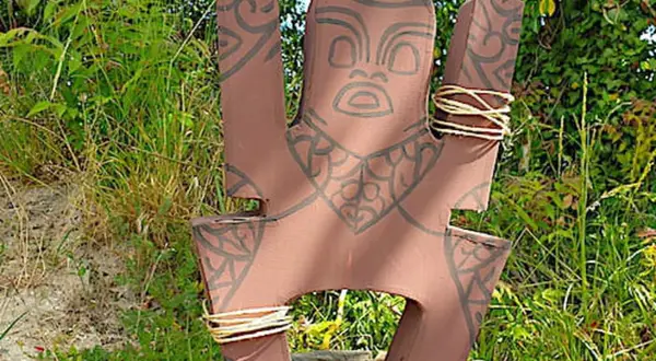 Modèle de totem à fabriquer, orné de motifs tribaux et de cordes. Il est posé dans un décor naturel verdoyant.