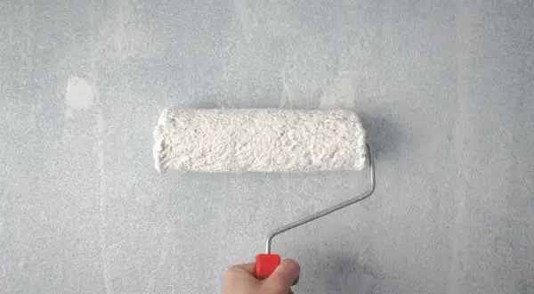 Main tenant, voici comment faire la peinture : un rouleau blanc couvre un mur bleu clair.