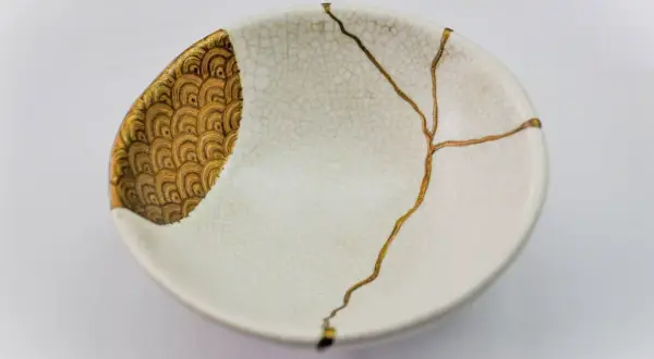Bol blanc orné de motifs dorés, réparé avec l'art japonais de la vaisselle cassée, soulignant la beauté des imperfections.