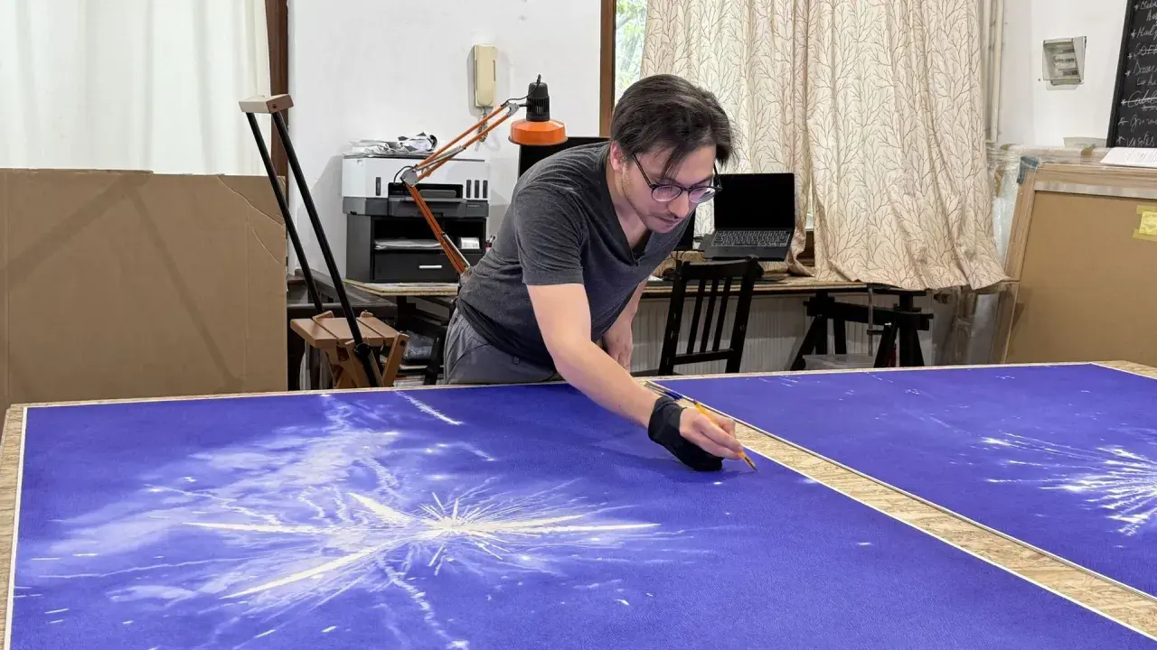 Un artiste stylo bic travaille sur une grande toile bleue, créant un motif d'étoiles filantes.
